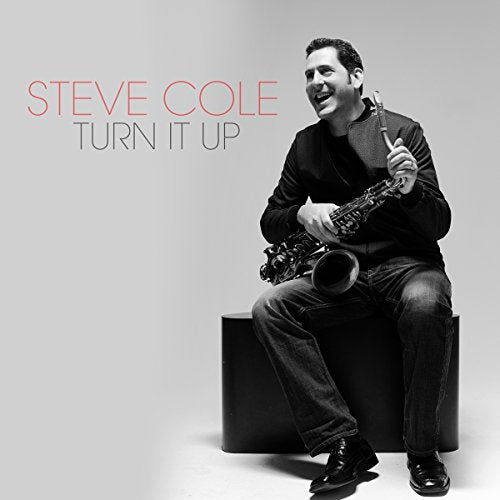 "Album cover with man holding saxophone, seated on a cube, against a gray background."