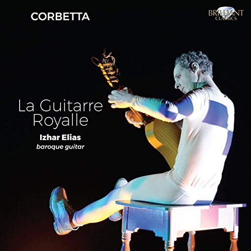 Man in white and blue outfit plays baroque guitar on a stool against a black background.