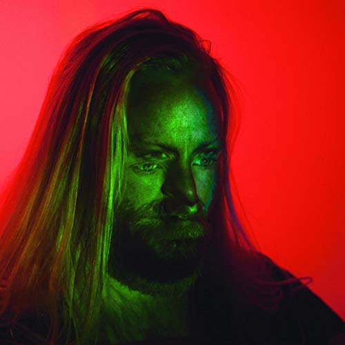 Close-up portrait of a man with long hair, lit with red and green.