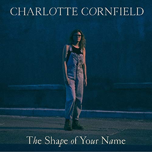 "Album cover featuring a woman in overalls standing in front of a dark blue wall."