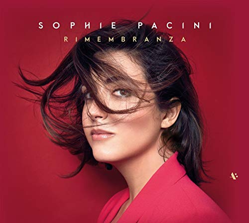 The image is a CD cover featuring a woman with dark hair and a red background. The woman is wearing a red blazer, and her hair is blowing in the wind. The title "Rimembranza" is written in white text at the top of the image, with the artist's name "Sophie Pacini" implied. To describe this image in a concise manner, the alt text could be: "A woman with blowing dark hair and a red blazer, against a red