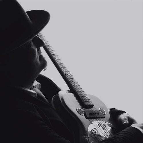 Man in hat holding guitar, black and white image, close-up of face and instrument.