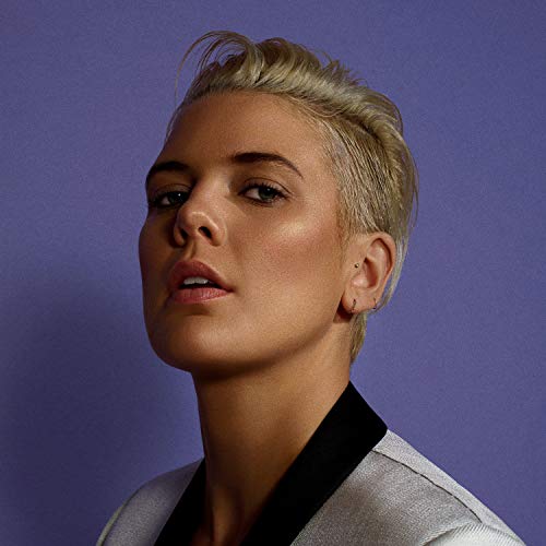 A woman with short blonde hair and a gray top against a purple background.