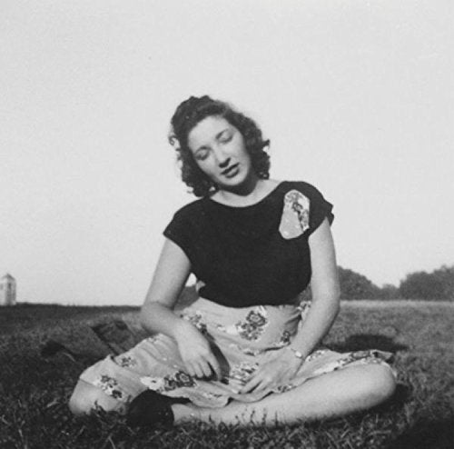 Black and white photograph of a woman sitting on grass, smiling and looking down.