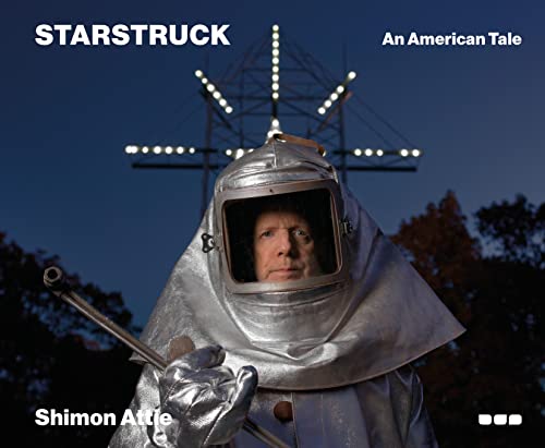 A person wearing a silver protective suit and helmet stands before a lit power tower.