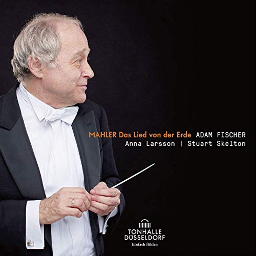 A man in a tuxedo holds a baton against a black background.