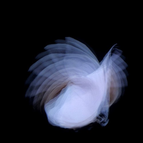 The image depicts a blurred white feather against a black background. Alt text: Blurred white feather on a black background.