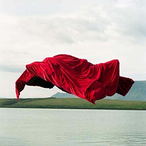 The image depicts a red fabric flowing over calm water and a green landscape.