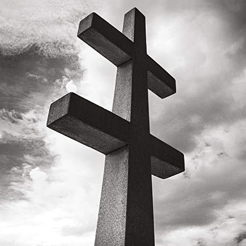 A large stone cross against a cloudy sky, depicted in black and white.