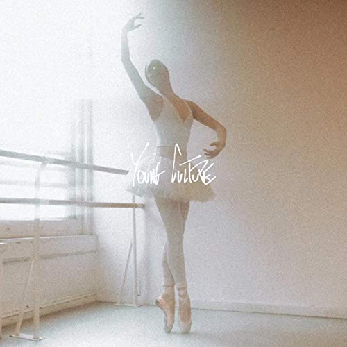 Ballet dancer in white attire and tutu standing in a studio with barre.