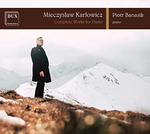Man in black coat stands on snowy hill, mountains in background, on album cover.