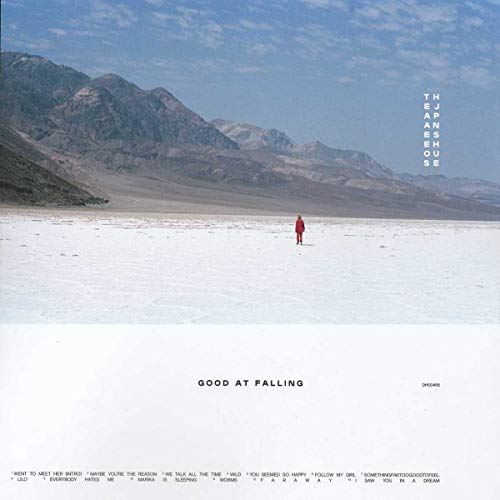 A person in red stands alone on a vast white salt flat, mountains in the background.