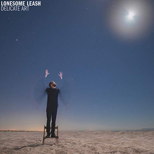 "Man standing on a stool in a desert under a starry night sky."