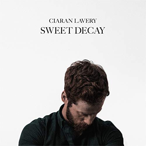 Album cover featuring a man with dark hair and beard, looking downward, against a white background.