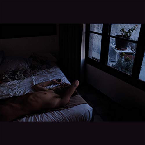 The alt text for the image is: "Nude man lying on a bed near a window."