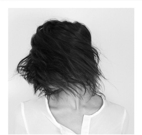 Black and white image of a woman's head and shoulders, hair covering her face.