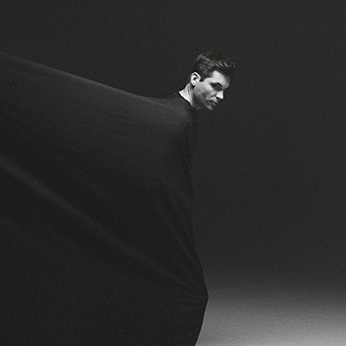 Man in black shirt, partially obscured by flowing black fabric, against dark background.