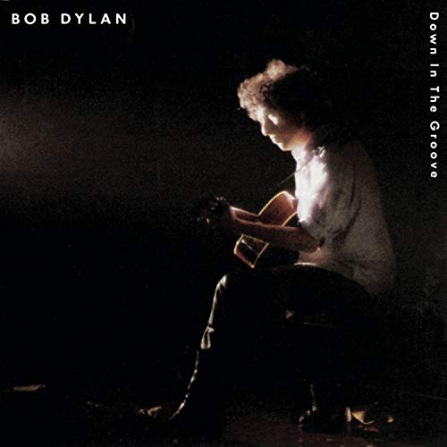Bob Dylan album cover featuring a man playing guitar on a stool in a dark setting.