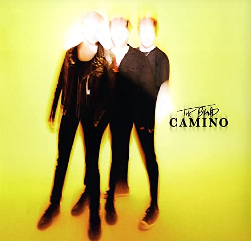 Blurred image of three people in dark clothing against a yellow background.