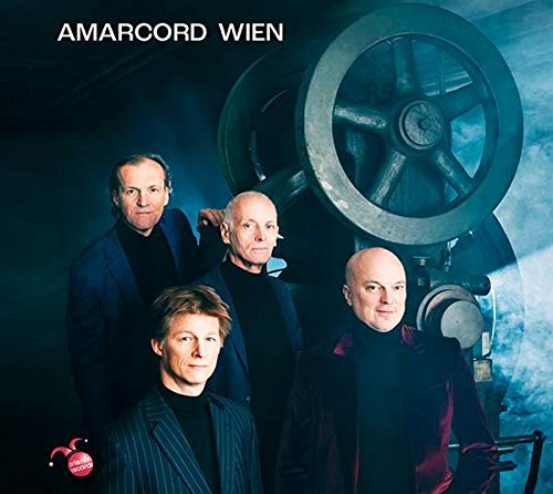 "Album cover with four men in dark attire standing by an industrial wheel."