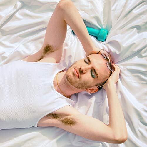 Man lying on white sheets, holding head with eyes closed, next to a teal bottle.