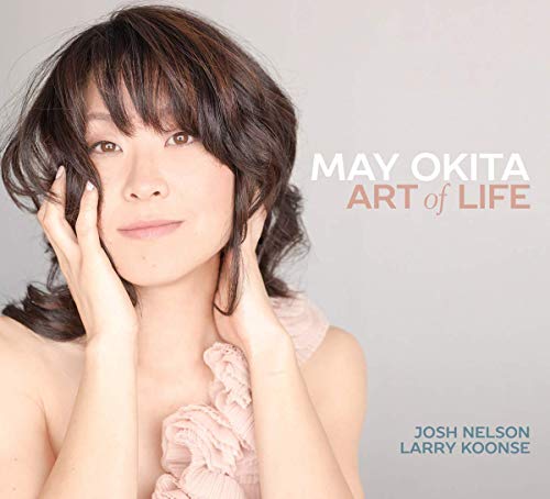 "Album cover featuring a woman with dark hair and a pink top, plain background."