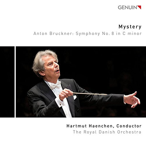 Conductor Hartmut Haenchen in a tuxedo, holding a baton, against a black background.
