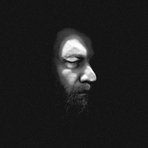 Black and white image of a man's face with a beard, surrounded by darkness.