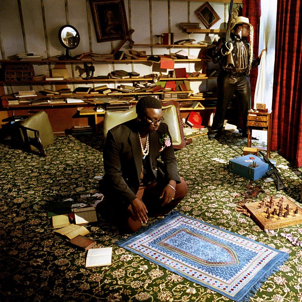 Compact disc with a man sitting on the floor in a cluttered room.