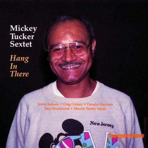 Album cover featuring a smiling man wearing glasses and a graphic t-shirt against a black background.