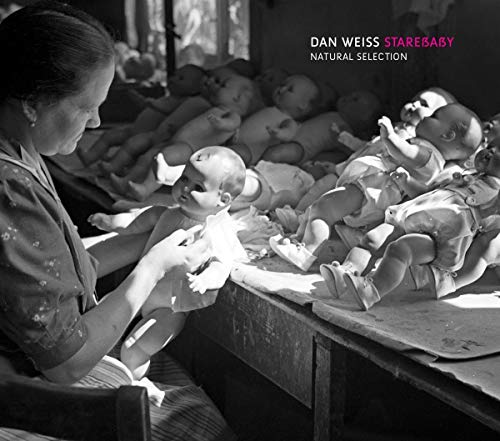 "Black and white album cover with a woman and multiple dolls on a table."