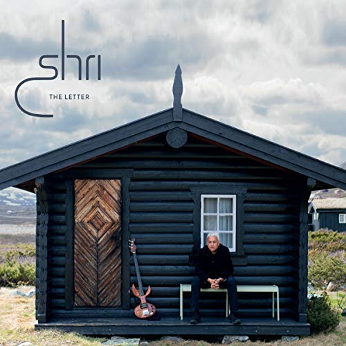 "Album cover: man sitting outside a log cabin with a guitar."