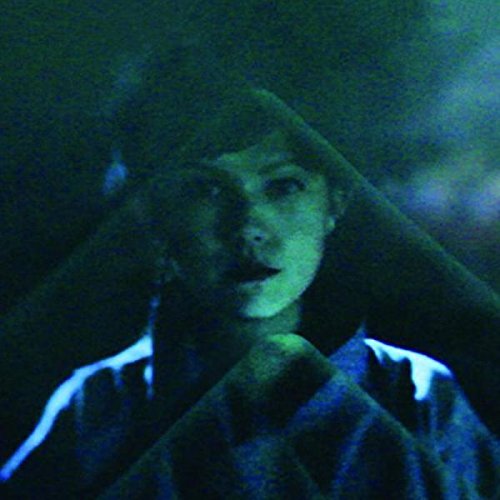 A woman wearing a dark hoodie with white stripes is shown in a dimly lit image.