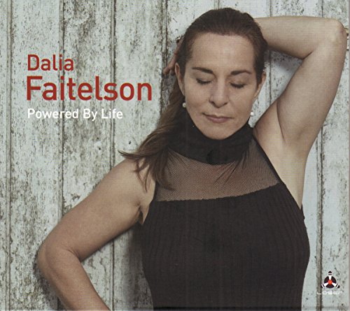 Woman in black top leaning against wooden wall, album cover for "Powered By Life" by Dalia Faitelson.
