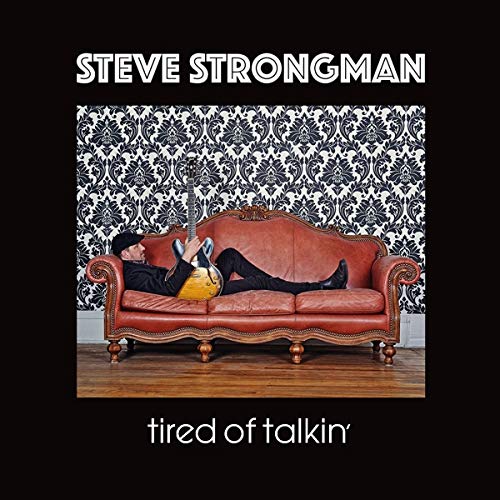 "Album cover featuring a man reclining on a red couch, holding a guitar."