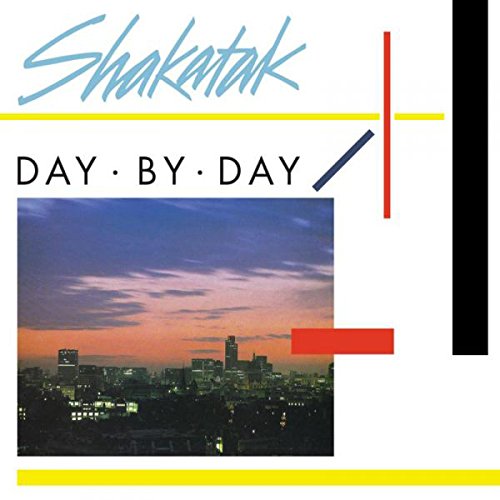 The image is a CD cover for the album "Day by Day" by Shakatak. The cover features a cityscape at dusk, with a prominent skyline and a vibrant sky. * **Title and Artist** * The title of the album, "DAY BY DAY", is written in black text below the artist's name. * The artist's name, "Shakatak", is written in blue cursive font at the top of the image. *