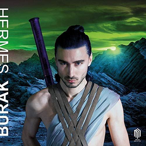 Man with dark hair and a staff, dressed in a toga, stands before rocky mountains.
