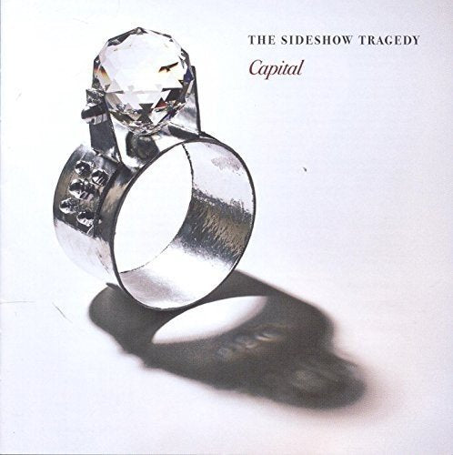 The image depicts the cover of a CD titled "Capital" by The Sideshow Tragedy. The cover features a large, silver ring with a clear gemstone on top, casting a shadow on a white background. The title and artist name are displayed in black text at the top right corner. Alt text: Silver ring with clear gemstone on white background, shadow cast below.