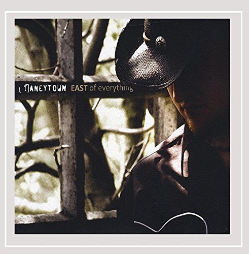 "Album cover featuring a man in a hat standing behind a metal grate."