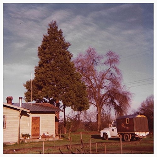 The image depicts a vinyl record cover featuring a small house and a truck. For accessibility purposes, a concise alt text could be: "Vinyl record cover with house and truck image."