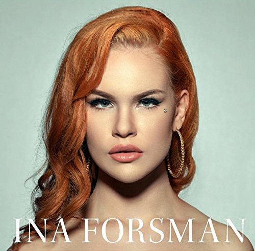 A woman with red hair and blue eyes looks directly at the camera.