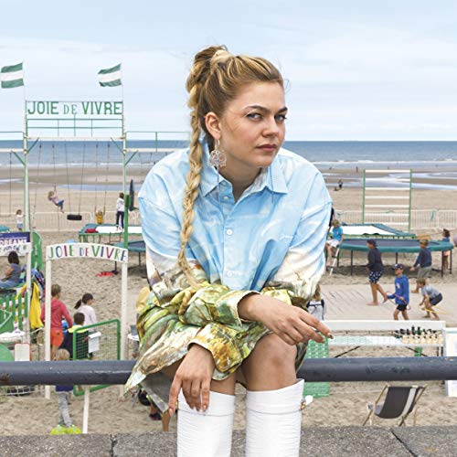 A woman with blonde braided hair leans on a railing at a beach volleyball court.