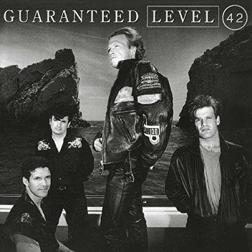 "Black and white album cover featuring four men posing in front of a rocky coastline."