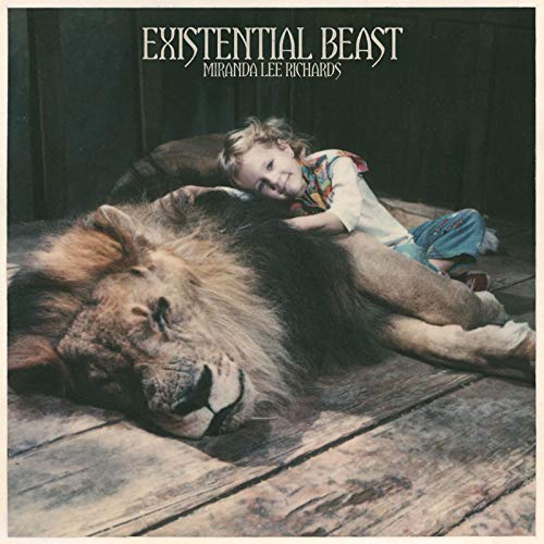 "Album cover with a child resting on a lion on a wooden floor."