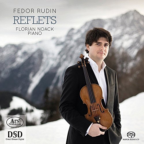 Man in a suit holding a violin, snowy mountains in the background.