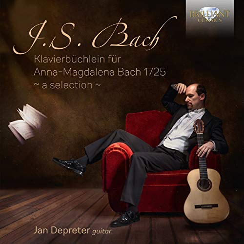 A man in a suit sits on a red chair with an acoustic guitar.
