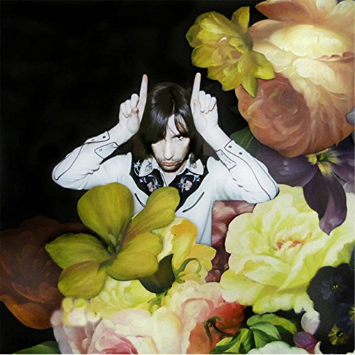 "Album cover featuring a man surrounded by flowers, pointing upwards against a black background."