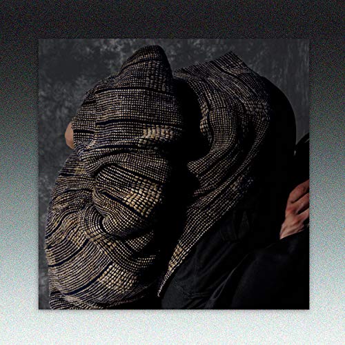 A person wearing a black and gold beaded head covering, holding a black object.