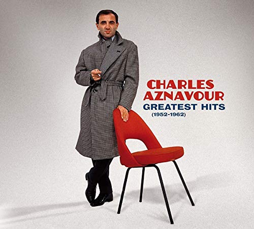 Charles Aznavour album cover with man in coat standing by red chair.