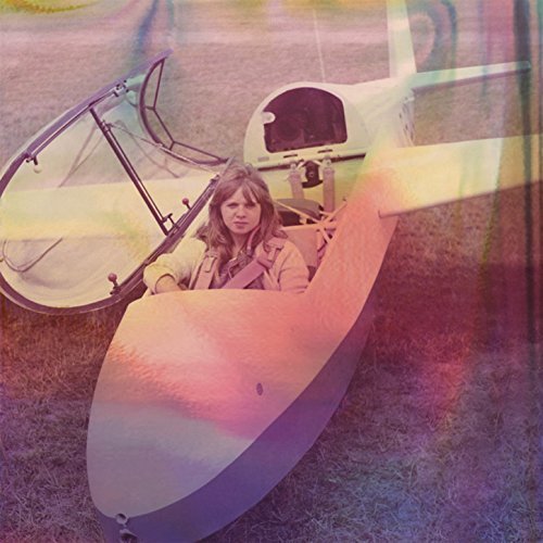 A woman sits inside a microlight aircraft on grass, wearing a light jacket.